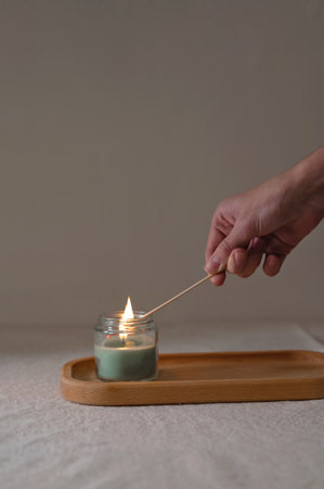 Person lighting a candle on a tray on faded beige background, minimal aesthetic backdrop, cozy home interior.の写真素材