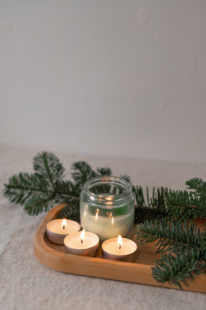 Aesthetic cozy winter home interior still life, candles with dim lights, fir branches on tray on table, with neutral beige empty wall background, soft focus, lifestyle.の写真素材