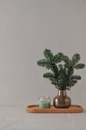 Minimal aesthetic winter home interior composition in Nordic style, vase with fir tree branch, green candle on wooden tray on table, neutral beige linen tablecloth and empty gray wall background.の写真素材