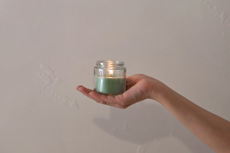 Woman hand holding green candle with soft dim light on neutral taupe beige wall background, minimal aesthetic concept.の写真素材