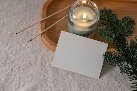 Paper card mockup, candle light and fir branch on tray, postcard or invitation template at home interior background.の写真素材