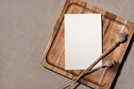 Elegant postcard or wedding invitation design template in bohemian or rustic style, blank paper card on brown wooden tray with poppy flower, empty linen neutral taupe beige background with copy space.の写真素材