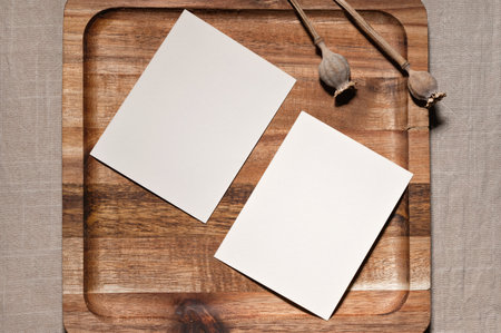 Two paper empty cards on brown natural wooden tray on neutral beige linen background, minimal elegant business template, flat lay, top view.の写真素材