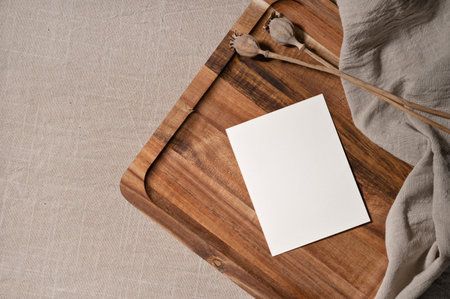 Empty greeting postcard or wedding invitation design template in bohemian style, blank paper card mockup on brown wooden tray, taupe beige linen cloth background, dried poppy flowers.の写真素材