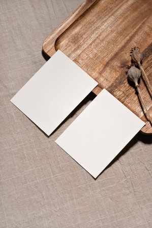 Two paper cards on beige tabletop with linen textured cloth background and wooden brown tray, mockup for business branding.の写真素材