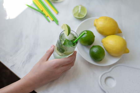 Fresh summer mojito cocktail drink in glass, lime, lemons and drinking straws on kitchen table, top view, lifestyle.の写真素材