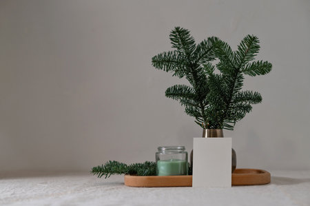 Minimal home interior composition, candle, vase with plant on wooden tray, empty paper card on table, empty neutral wall background, natural light.の写真素材