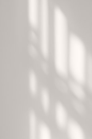 Elegant natural aesthetic backdrop, soft blurred sunlight shadow pattern of windowpane on neutral gray beige plaster wall backgroundの写真素材