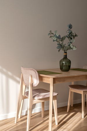 Warm cozy dining room in Mediterranean style, light beige wooden table and chairs, green vase with olive tree branch, natural sunlight shadows on beige wooden wall, modern apartment interior designの写真素材