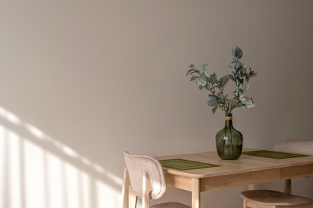Warm sunny aesthetic Mediterranean dining room or kitchen interior, wooden table and armchairs, green vase with olive plant, empty neutral beige wall background with natural sunlight shadowsの写真素材