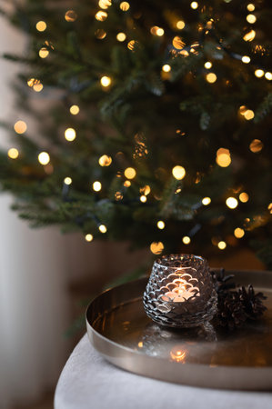 Aesthetic Christmas holiday background, candle light on cooper tray, green Christmas tree with shining lights boke on background, luxury home interior decor in dark brown and green tonesの写真素材