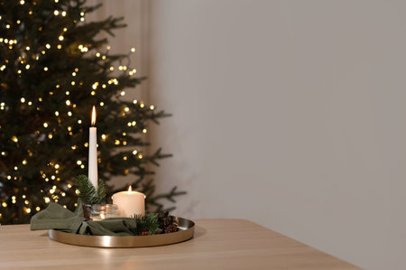 Candle lights burning on table, blurred Christmas tree with shining lights and empty neutral beige wall background. Minimal aesthetic holiday interior decor, lifestyle real home, blank copy spaceの写真素材