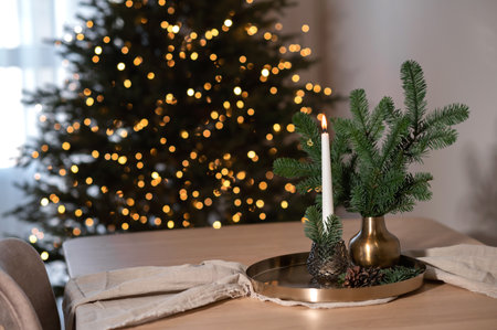 Aesthetic Christmas holiday home interior, beige wooden table, candle light and vase on cooper tray, linen table runner, blurred Christmas tree shining light on backgroundの写真素材