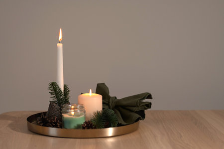 Beautiful cozy candlelight backdrop with empty copy space, aesthetic Christmas still life with lit candles and fir tree branches on tray on neutral beige wooden table backgroundの写真素材
