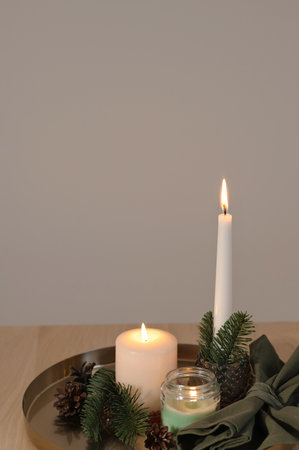 Candlelight, minimal aesthetic Christmas home interior decor, candles burning, fir tree branches on tray on beige wooden table, empty neutral wall background, copy spaceの写真素材