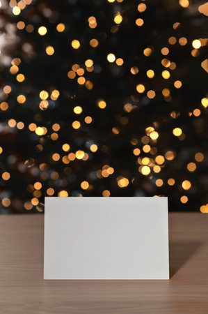 Festive greeting postcard mockup, blank paper card on table, blurred Christmas golden shining lights bokeh on background.の写真素材