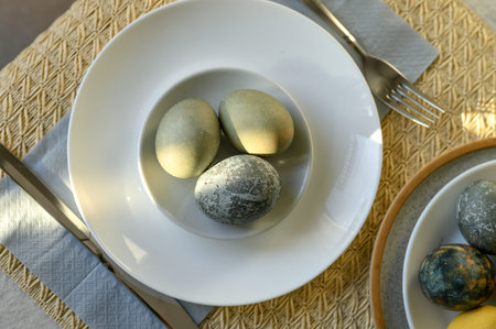 Yellow, green, blue gray natural colored Easter eggs on plate serving for holiday dinner,...