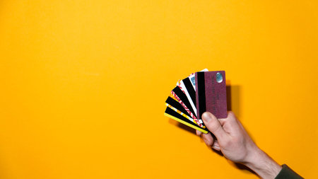 Bright yellow background with hand fanning several credit cards. Retail, consumerism and financial...