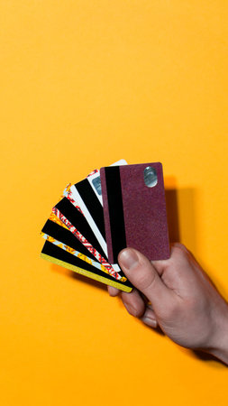 Close-up vertical composition of hand holding multiple bank cards against vibrant yellow background....