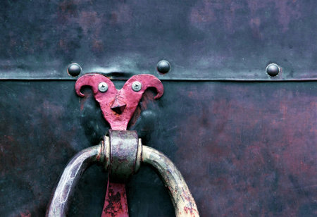 A metal door with a playful handle in the form of a jester. Old metal, rusty door of different colors.の写真素材