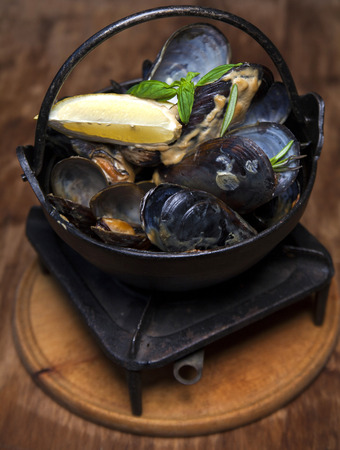 mussels with lemon and basil in an iron saucepan on a wooden tableの写真素材