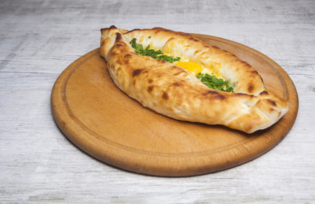 khachapuri on with egg and greens lies on a wooden tableの写真素材
