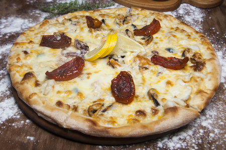 pizza with seafood, dried tomatoes and cheese on a wooden table covered with flour with a rosemary branchの写真素材