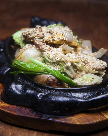 fried pork with sesame and green onions in an iron plate on a brown wooden tableの写真素材