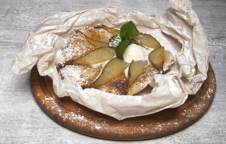 tart with pear, cinnamon and ice cream in paper on a brown wooden standの写真素材