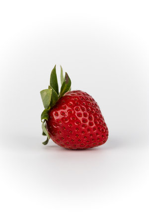 closeup on a white photo background lies one ripe strawberry in the center of the background healthy vitamins seasonal summer fruit green strawberry tail like a crownの写真素材