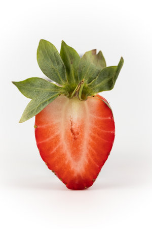 close up on a white photo background there is a cut half of a ripe strawberry suspended in the air healthy vitamins seasonal summer fruitの写真素材