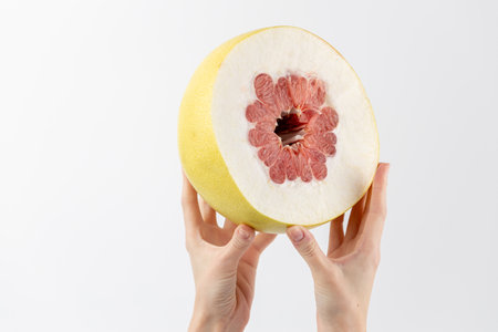 on a white photo background, thin female hands hold a large fruit, cut in half, a little pulp, thick skin, tropical yellow fruit, healthy vitamins, seasonal fruit, vitamin Cの写真素材