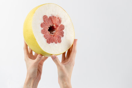 on a white photo background, thin female hands hold a large pamella fruit, cut in half, a little pulp, thick skin, tropical yellow fruit, healthy vitamins, seasonal fruit, vitamin Cの写真素材