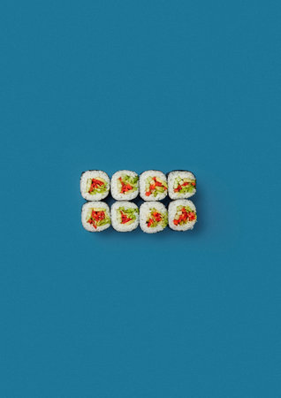 on a blue background lies a set of sushi with rice and fresh vegetables wrapped in a sheet of nori