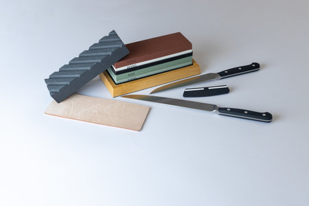 white background on stand lies all the equipment a set for sharpening and polishing kitchen knives and various blades different abrasiveness of stones retainer for knives sheet tanned leather knivesの写真素材