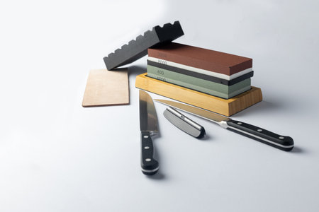 white background on stand lies all the equipment a set for sharpening and polishing kitchen knives and various blades different abrasiveness of stones retainer for knives sheet tanned leather knivesの写真素材