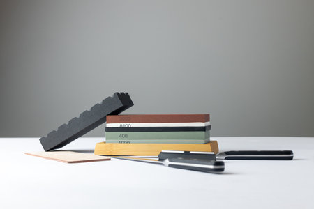 white background on stand lies all the equipment a set for sharpening and polishing kitchen knives and various blades different abrasiveness of stones retainer for knives sheet tanned leather knivesの写真素材