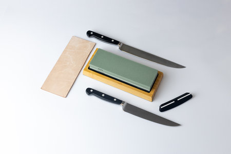 white background on stand lies all the equipment a set for sharpening and polishing kitchen knives and various blades different abrasiveness of stones retainer for knives sheet tanned leatherの写真素材