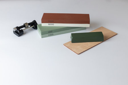 white background on table lies all the equipment a set for sharpening polishing kitchen knives and various blades different abrasiveness of stones retainer for knives sheetの写真素材