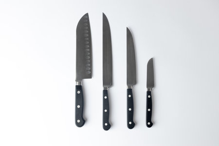 on a white background on a table lie steel straight kitchen knives of different calibers and sizes with a black handle, a set for various purposesの写真素材