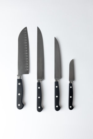 closeup white background on a table lie steel straight kitchen knives of different calibers and...