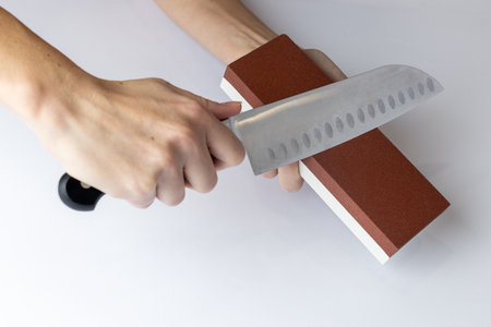 closeup on a white background on a table, women's hands sharpen a steel knife, a lock under the arm,...