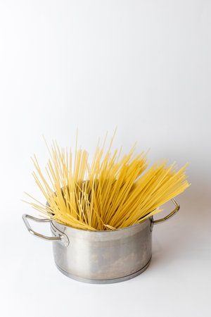 close-up on a white background, carefully laid out yellow spaghetti lies in an iron casseroleの写真素材