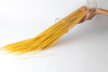 on a white background from the side of a female thin hand holding a transparent container with spaghetti for storing cereals white lid with fixationの写真素材