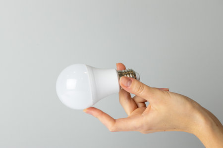 close-up on a white background from the side, a woman's thin hand holds a white light bulb with a wide base, neutral color, lighting elementの写真素材