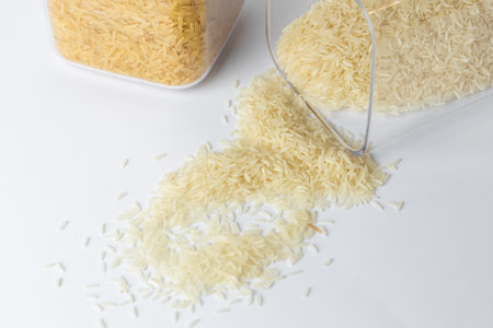 close-up on white stand of different sizes two transparent containers with white lids filled with different rice white rice and basmati minimalism spilled rice on table from a containerの写真素材