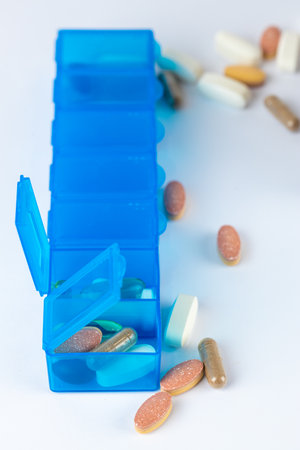 closeup white background two bright blue pill boxes with a couple of open lids for taking pills, health care, partial filling different shapes colors of pills and vitamins pills lie next to the tableの写真素材