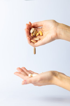 white background on outstretched palms of women hands, pills and vitamins of different shapes and colors are transferred from hand to palm health care pills in the airの写真素材