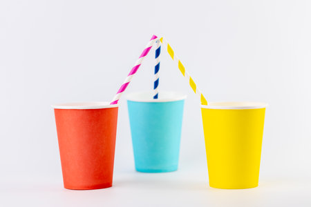on white background there are three paper cups next to each other yellow red and blue with matching paper cocktail straws inside disposable tablewareの写真素材