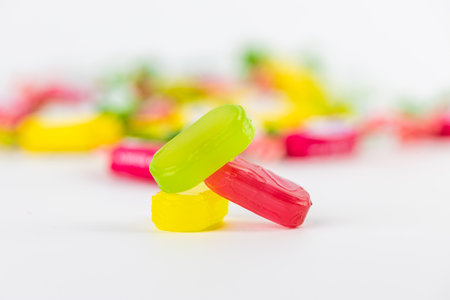 closeup on white background lie three caramel candies green pink yellow on the background of candies a lot of sugar development of diabetes and caresses sweets for childrenの写真素材
